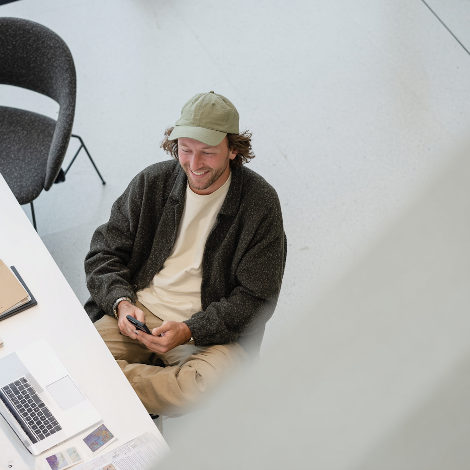 A man smiling at his phone while researching at a desk with a laptop