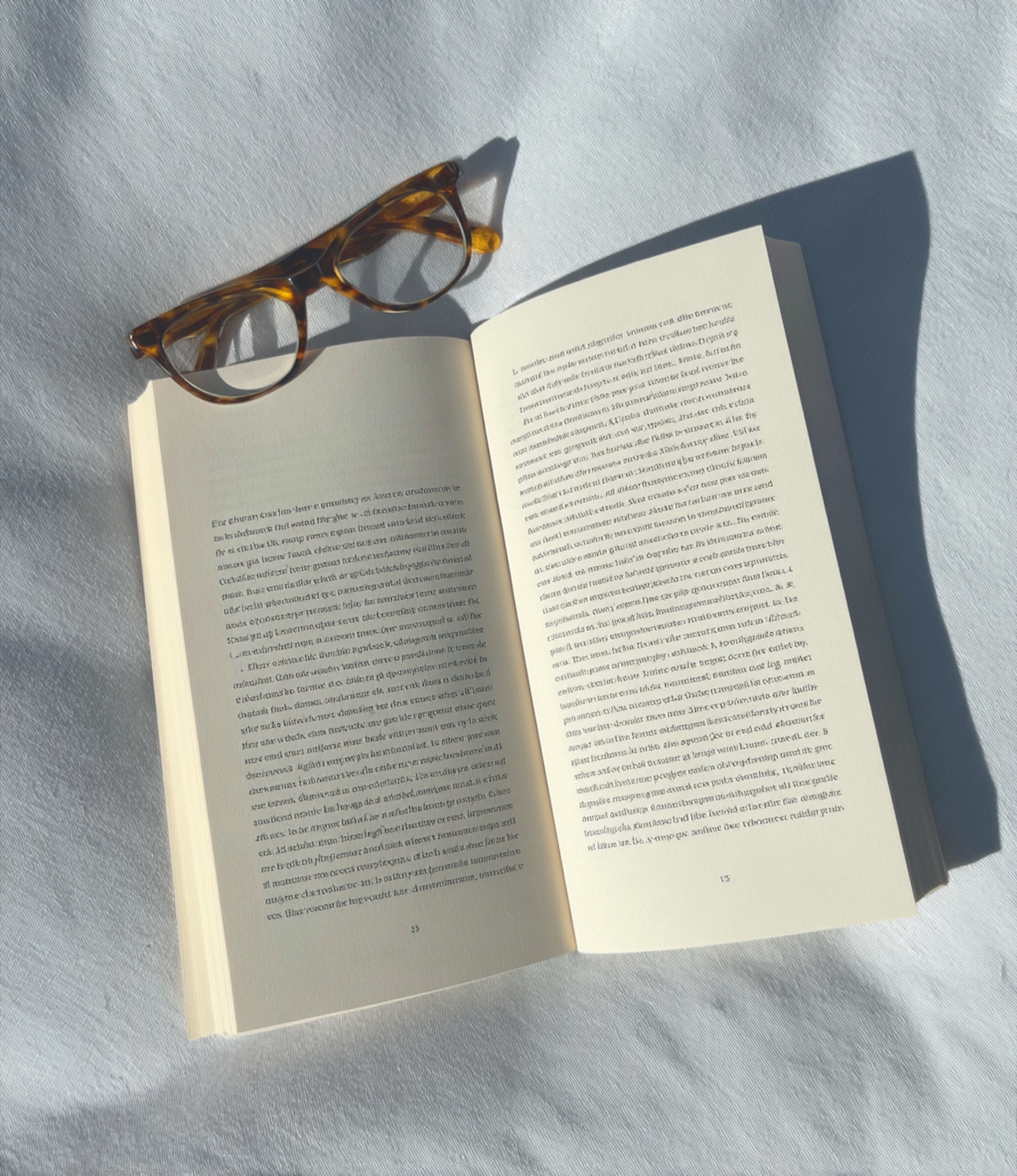 An open book with reading glasses resting on it in soft sunlight