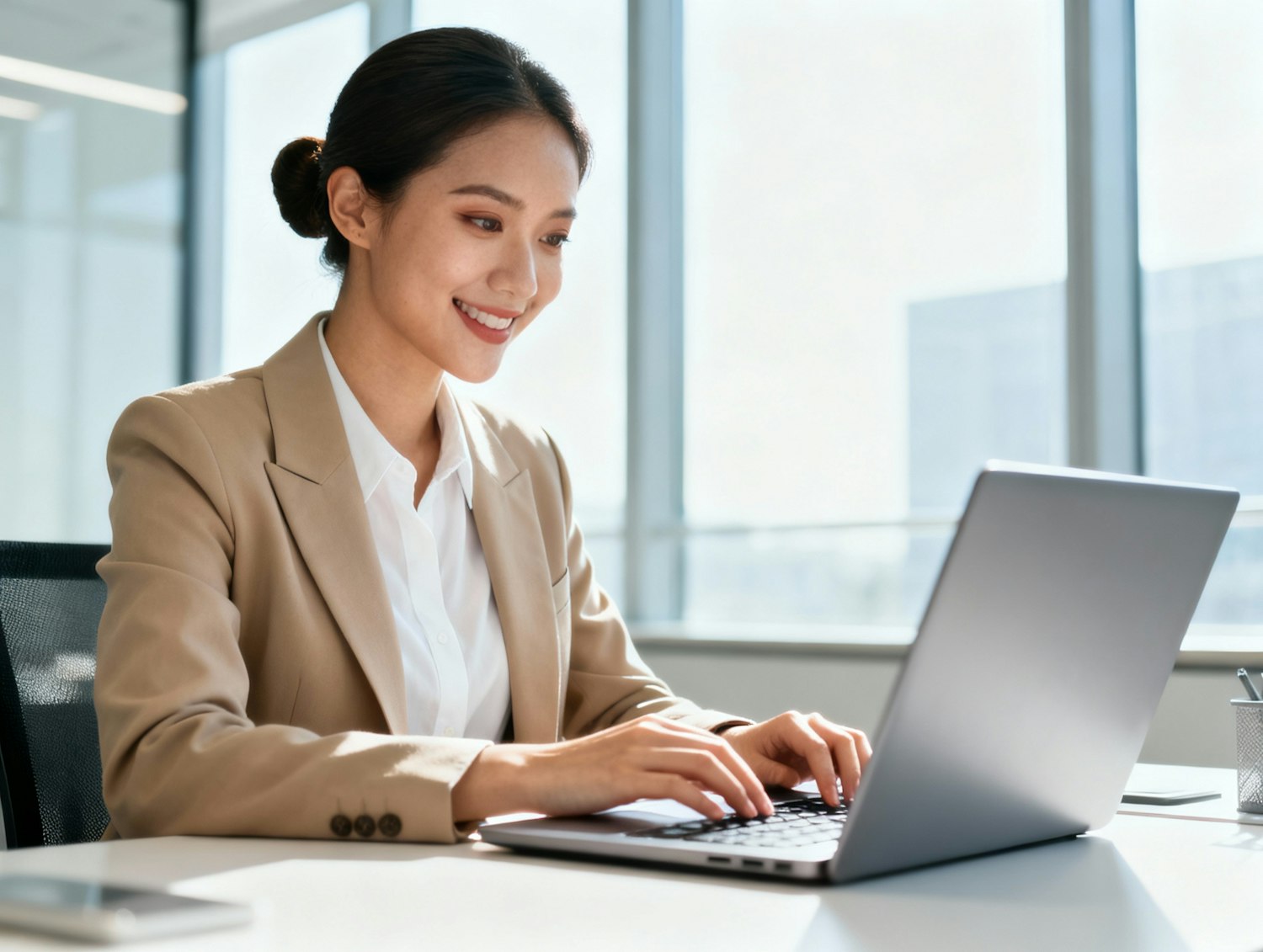 Smiling attorney in a beige blazer working on a laptop by a bright office window